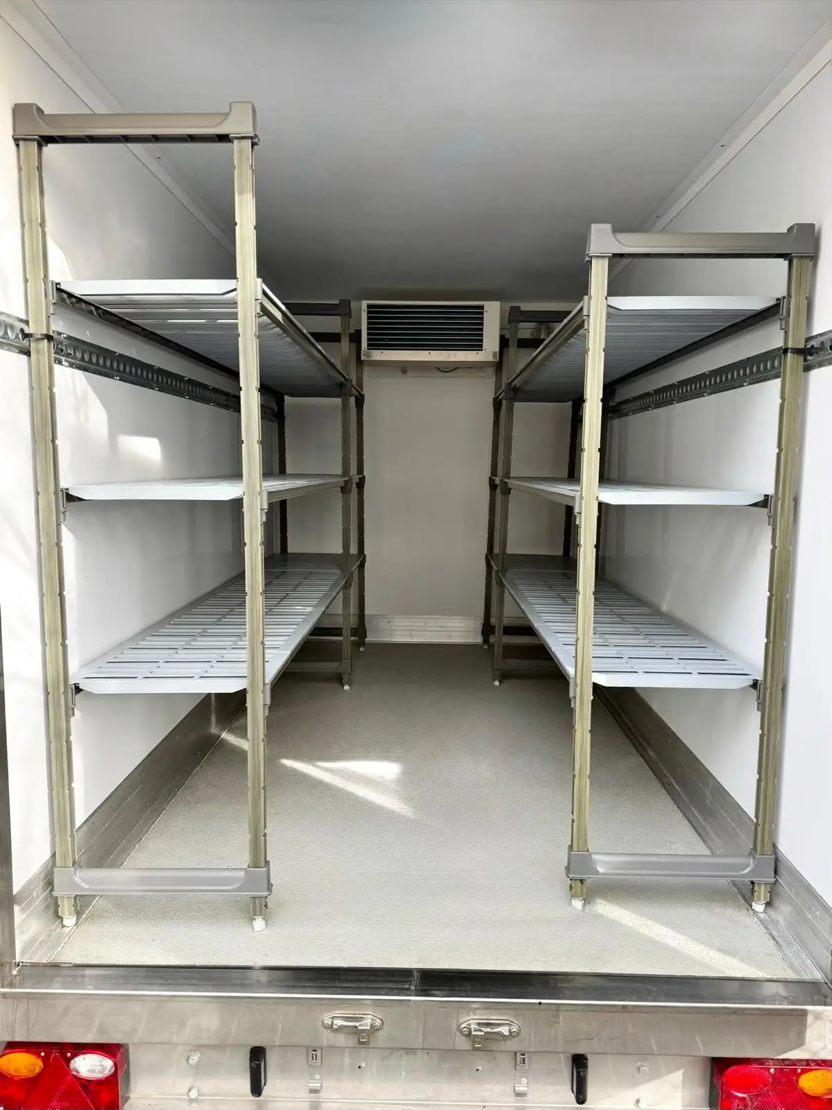 Interior of a fridge trailer showing metal shelving units and ceiling-mounted cooling unit, available for fridge and freezer trailer hire.