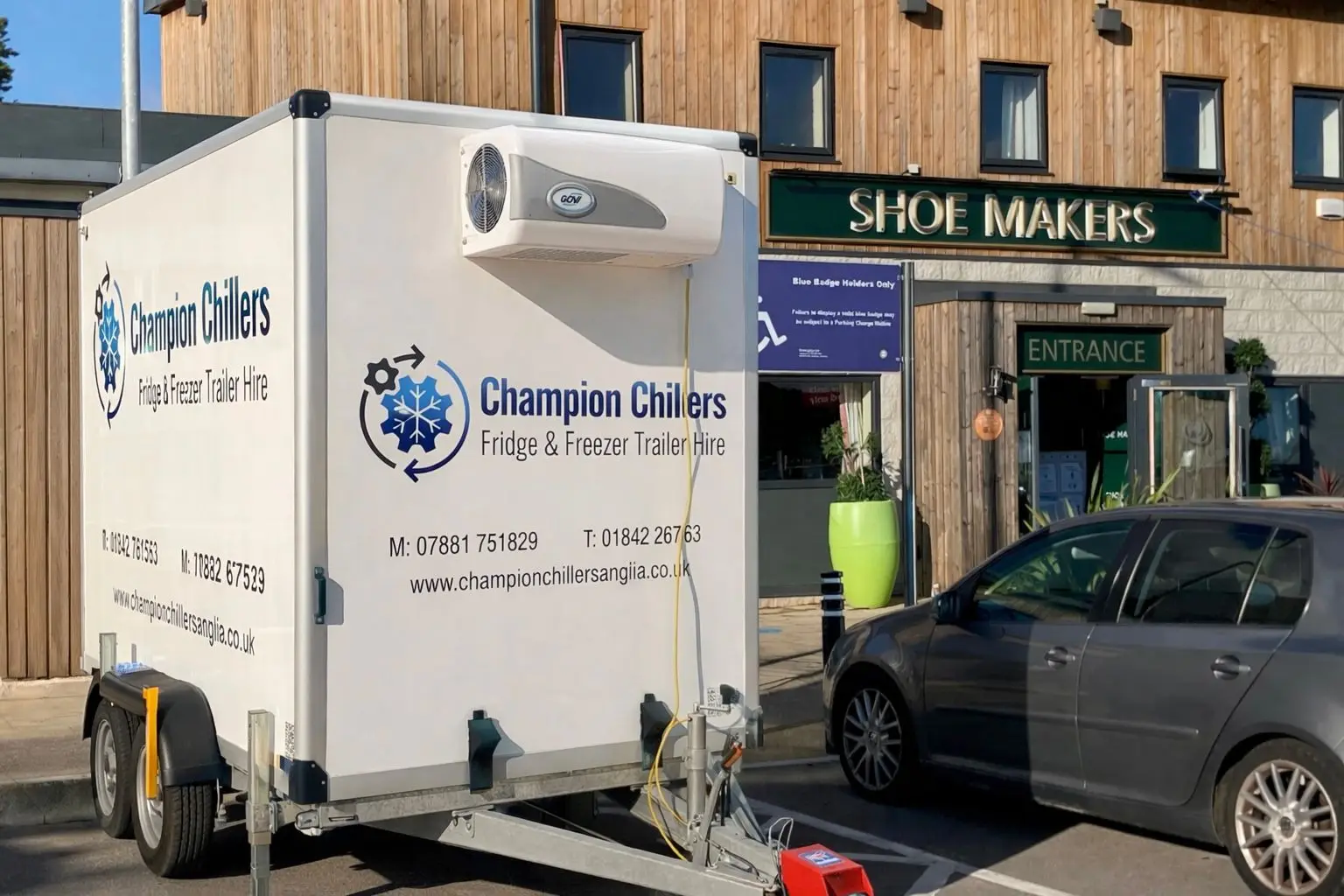 Champion Chillers fridge and freezer trailer hire unit parked outside a shop, branded with logo and contact details.