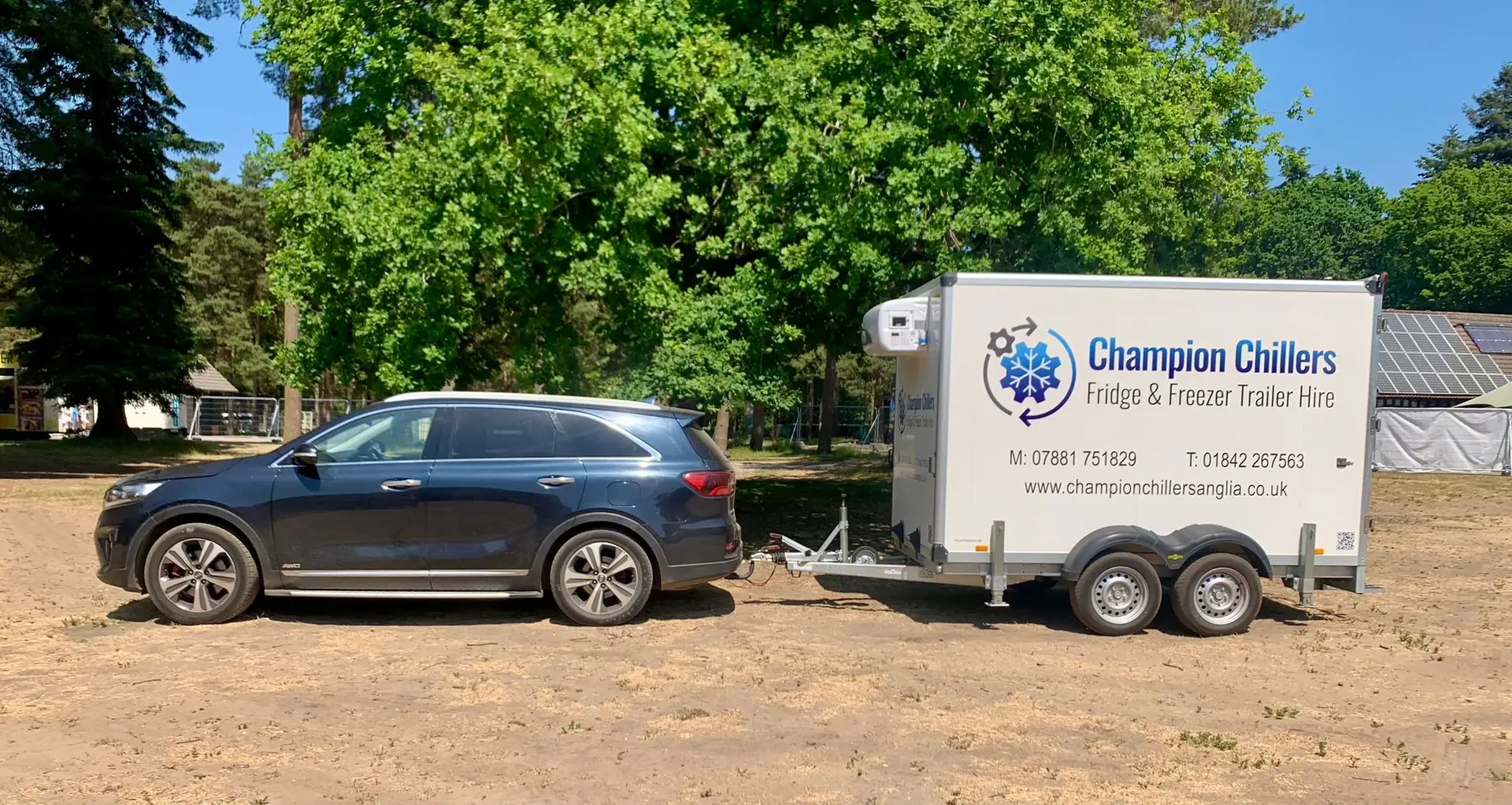 Car towing a Champion Chillers fridge and freezer trailer hire unit onto an event site.