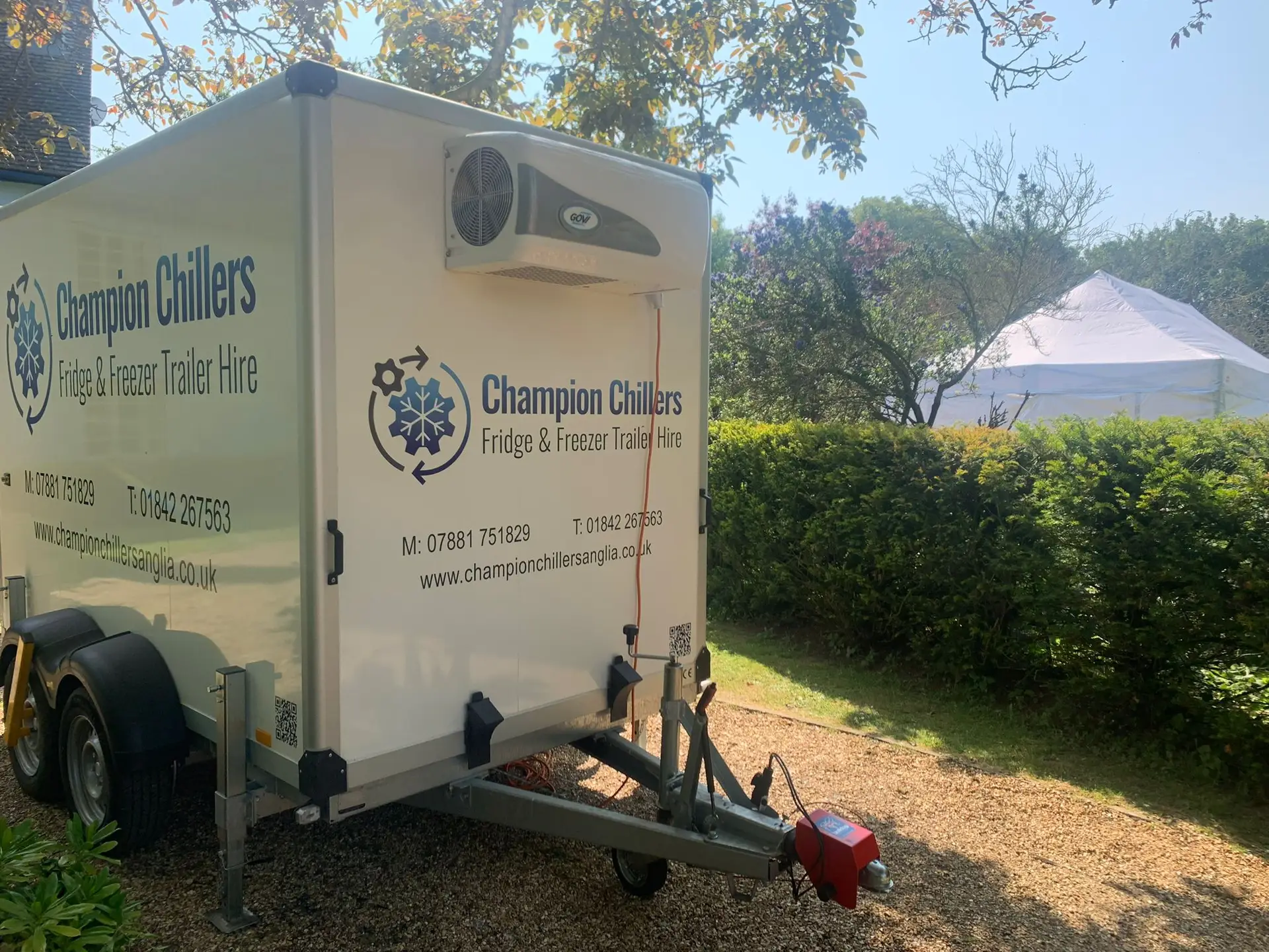 Champion Chillers fridge and freezer trailer hire unit on a gravel driveway, with a marquee visible over the hedge.