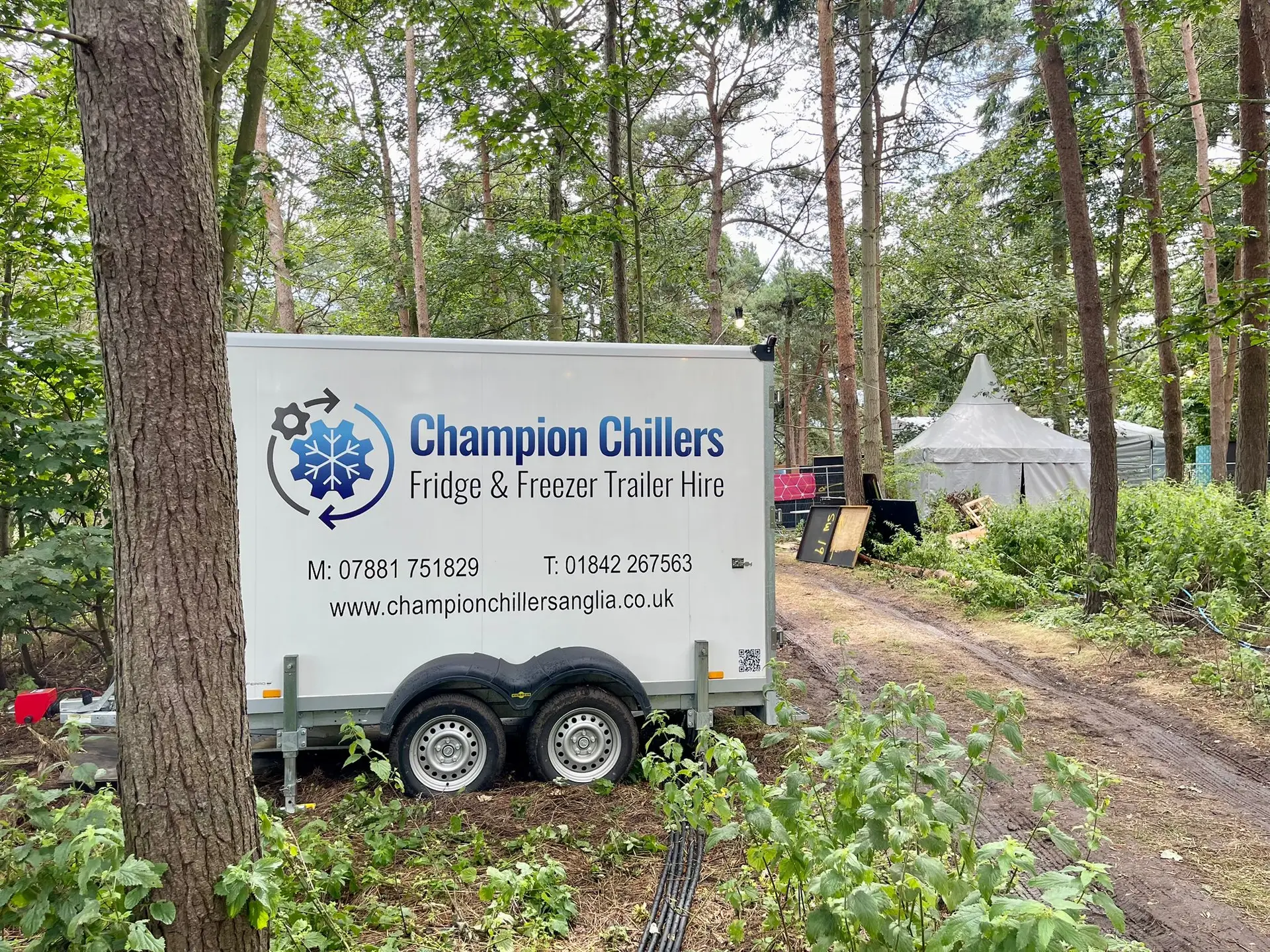 Champion Chillers fridge and freezer trailer hire unit parked in woodland at a festival site.
