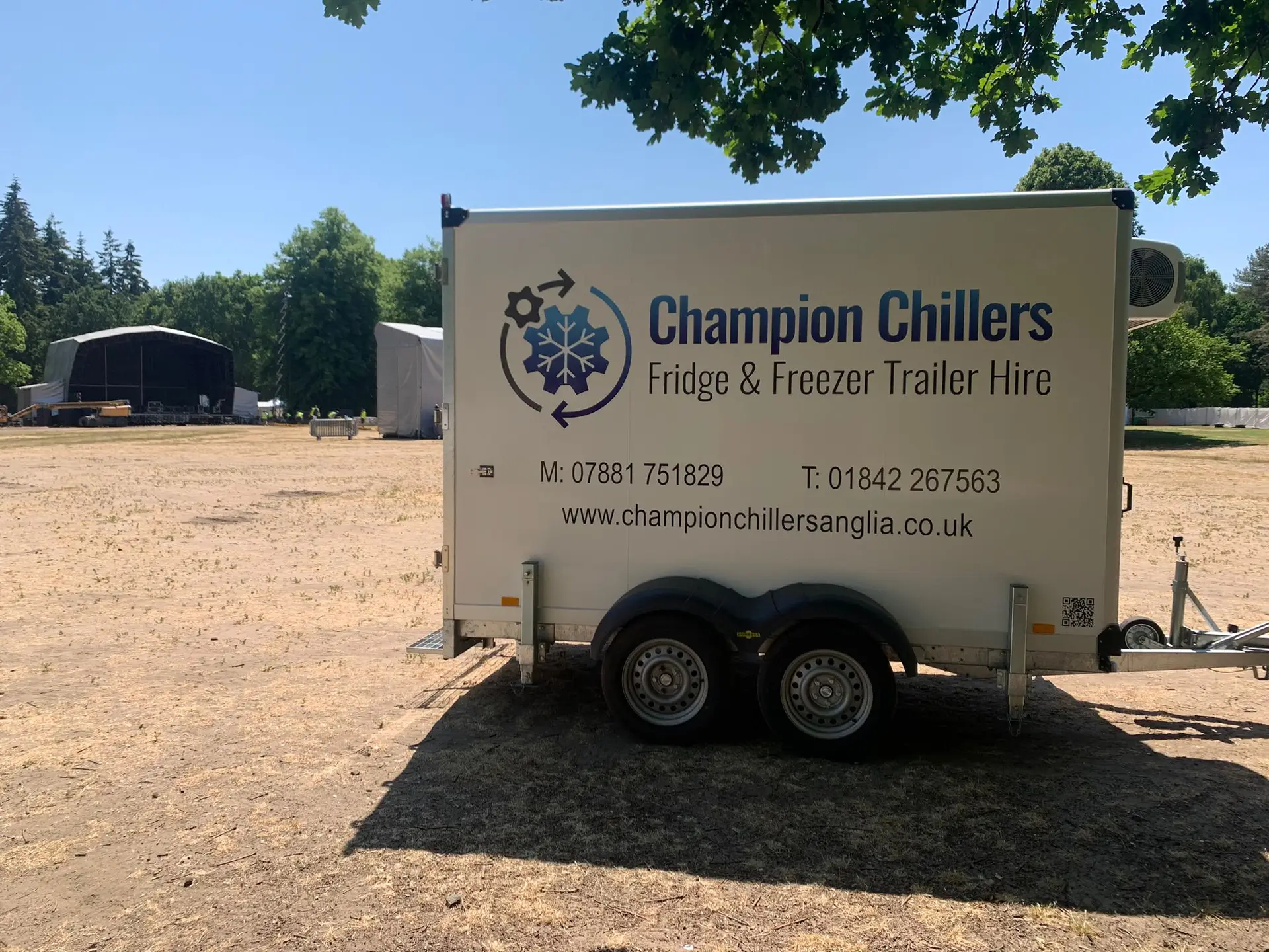 Champion Chillers fridge and freezer trailer hire unit on a field with a festival stage being built behind.