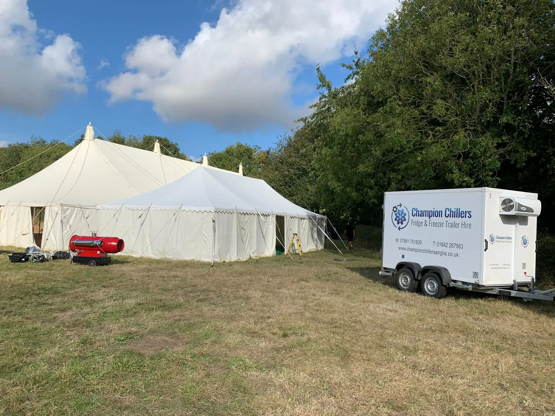 Champion Chillers fridge and freezer trailer hire unit set up on grass next to a marquee being prepared for an event.