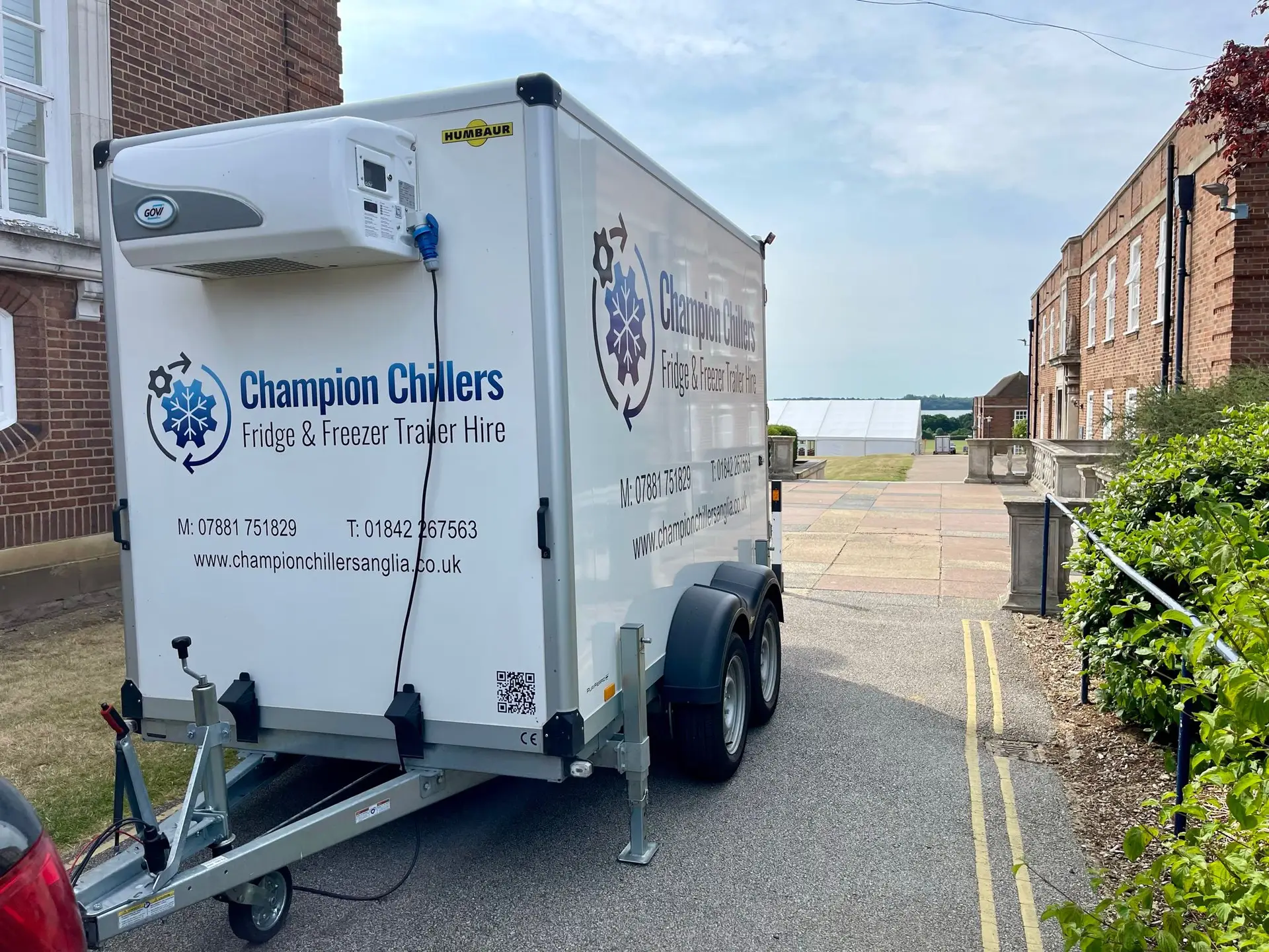 Champion Chillers fridge and freezer trailer hire unit parked outside a period building, with a marquee visible beyond.